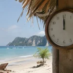 Une horloge murale affiche midi devant une plage thailandaise