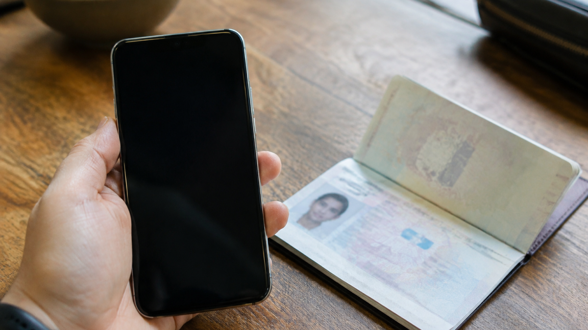 Main tenant smartphone devant passeport ouvert sur table