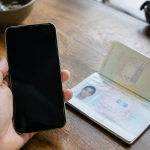 Main tenant smartphone devant passeport ouvert sur table