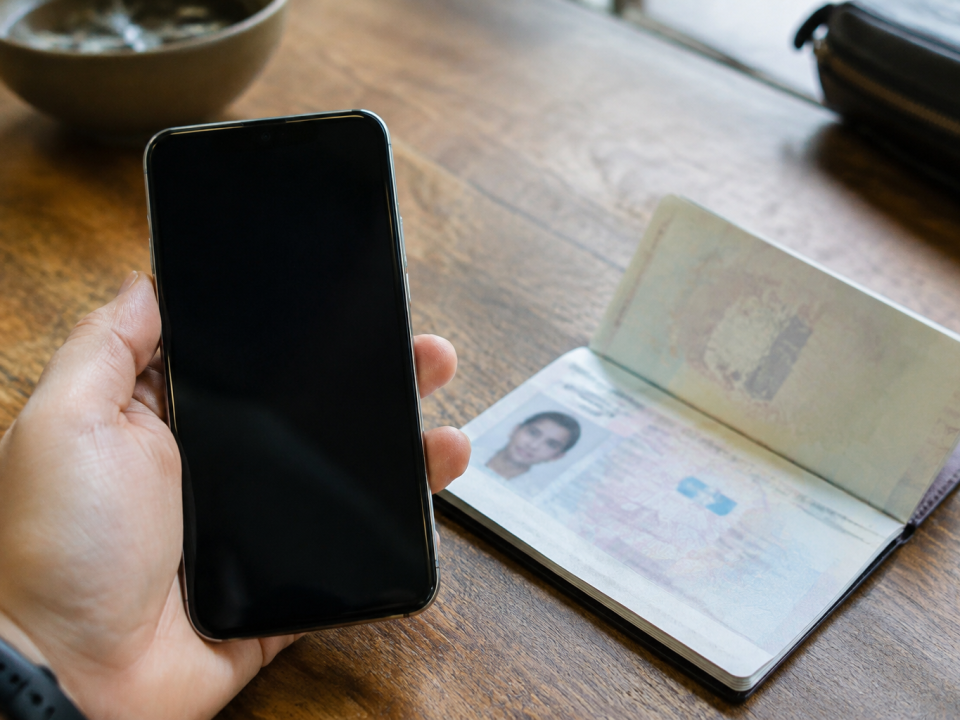 Main tenant smartphone devant passeport ouvert sur table